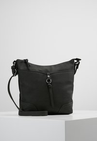 Sac en cuir noir à bandoulière avec fermeture éclair, sommet incurvé, surface texturée et sangle ajustable. Détail distinctif : un élément métallique central.