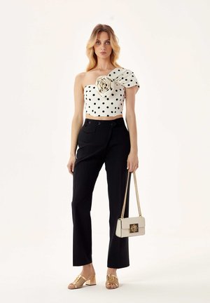 White polka dot crop top with one shoulder and floral detail, paired with high-waisted black trousers and gold, block-heeled sandals.