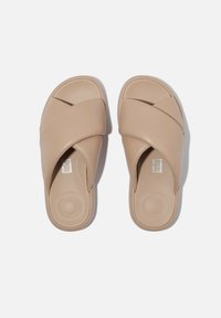 Beige schuifsandalen hebben een cross-strap ontwerp gemaakt van glad synthetisch materiaal met een gevoerd voetbed en een ronde zool.