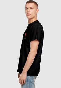 Black cotton t-shirt with short sleeves, featuring a red heart graphic and text on the front. Casual fit; smooth, lightweight fabric.