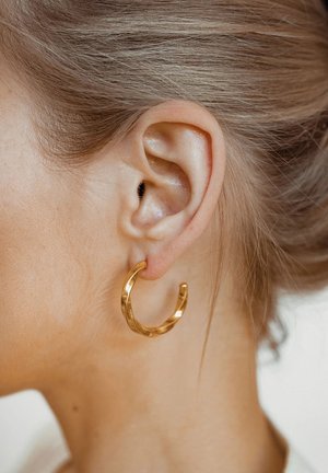 Goldene Creolenohrringe mit einem gedrehten Design. Der Ohrring zeigt eine glänzende, reflektierende Oberfläche mit einer kreisförmigen Form.