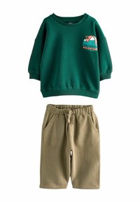 Sweat à capuche vert avec une montagne et le texte "Aventure en plein air"; associé à un short beige clair doté d'une taille élastique et de poches.