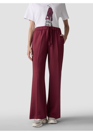 Person wearing burgundy wide-leg pants with drawstring waist, white sneakers, and a white t-shirt with a sketch of a woman in a red jacket.