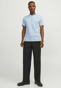 Camisa henley de manga corta azul claro con tres botones, combinada con pantalones de pierna ancha negros y zapatos negros. Diseño simple y limpio.