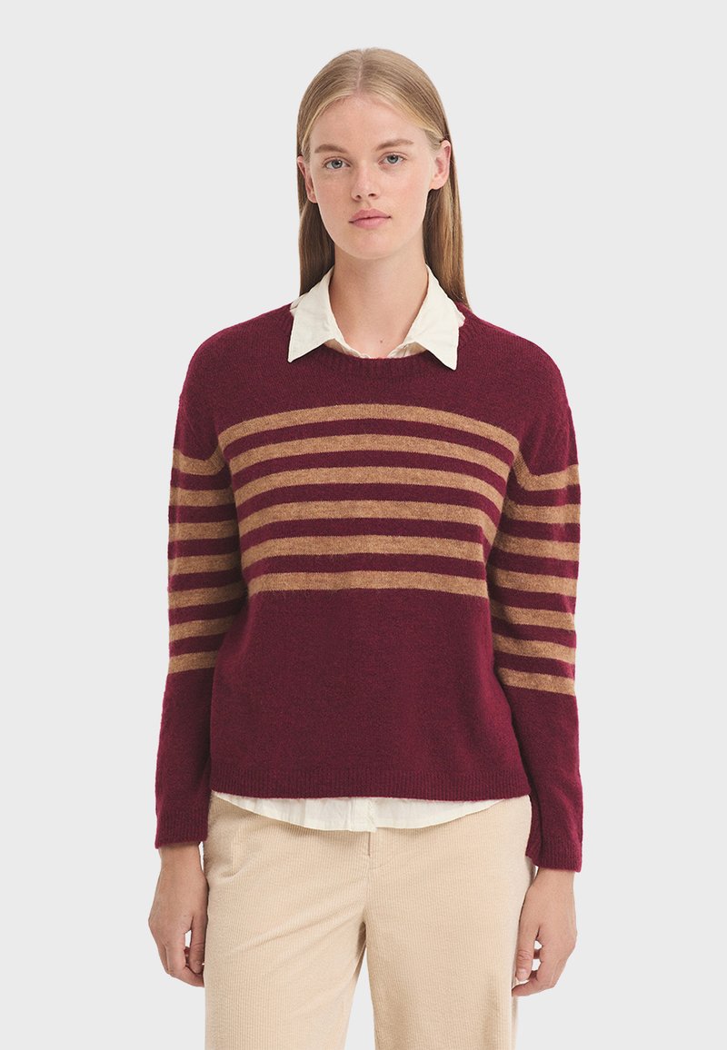 Maglione pullover bordeaux con righe orizzontali marroni, scollo rotondo e vestibilità rilassata. Tessuto morbido, indossato sopra una camicia bianca con colletto.
