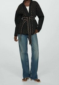 Czarna katana w wzory z zawiązywanym paskiem, zestawiona z luźnymi niebieskimi dżinsami. Miękka tkanina z delikatnym połyskiem i unikalnymi zdobieniami.