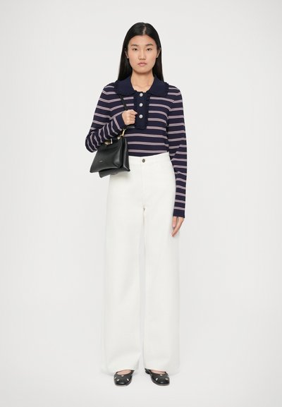 Chemise rayée bleu marine et blanche à manches longues avec un col volanté, associée à un pantalon large blanc taille haute et des chaussures à pois noirs.