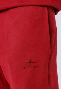 Joggers de ante rojo con bolsillos laterales, presentan un logo PXP bordado en tonos. Textura suave con un ajuste entallado y costuras cuidadas.