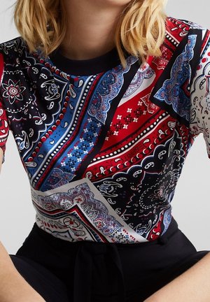 Haut à manches courtes présentant un motif cachemire multicolore en noir, rouge, bleu et blanc, avec un col rond et une texture douce.