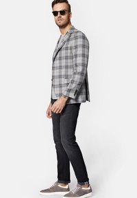 Szary marynarka w kratę, o dopasowanym kroju i klapach z wycięciem. W połączeniu ze szarymi dżinsami i casualowymi szarymi trampkami. Na nosie czarne okulary przeciwsłoneczne.