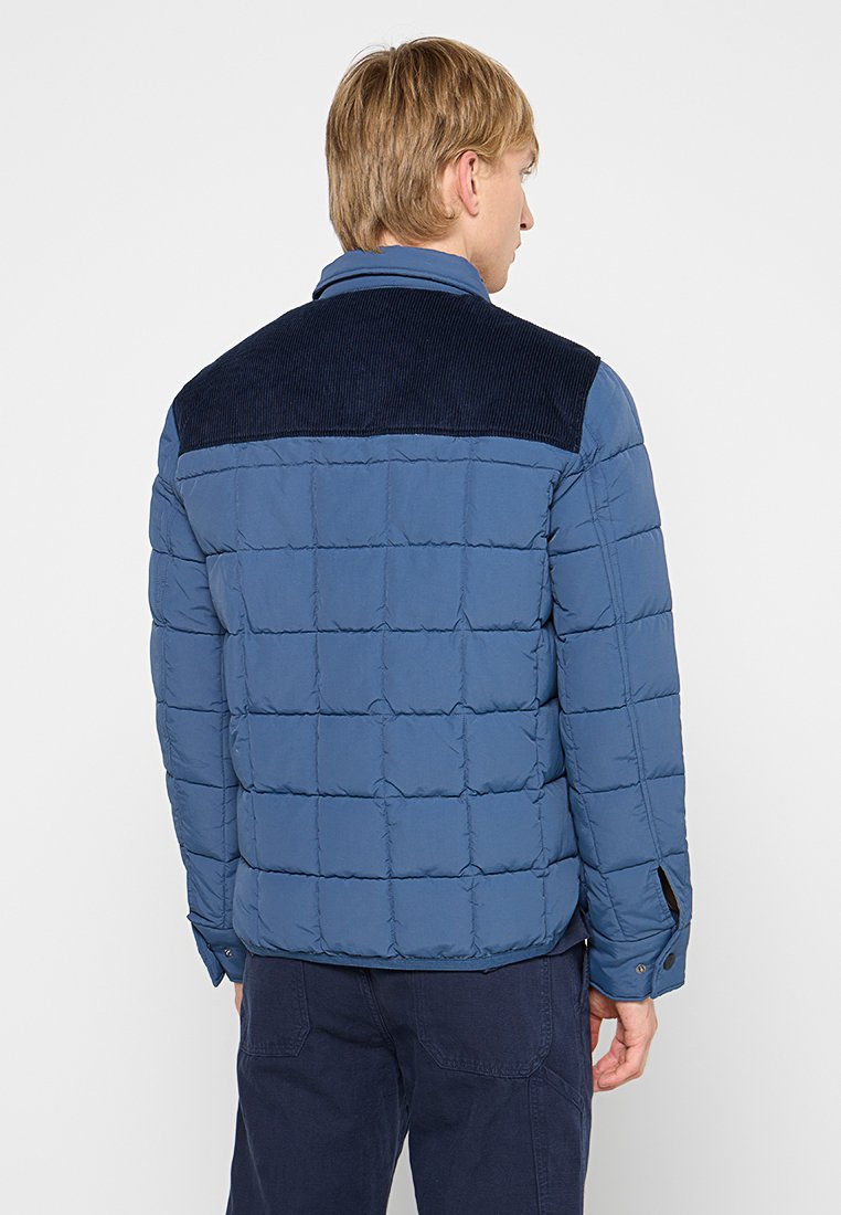 Giacca a vento blu con design trapuntato e dettagli in corduroy sulle spalle; presenta un collo con revers e polsini con bottoni.