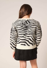 Zwart-witte gestreepte trui met een gestructureerd breisel, ronde hals en geribbelde zoom. Gecombineerd met een zwarte rok.