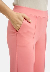 Light pink pants with a smooth texture, featuring side pockets and a wide elastic waistband. Subtle stitching details enhance the design.