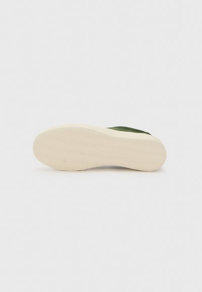 Adidași din suede verde, cu o suprafață texturată și o talpă groasă din cauciuc crem, având un model în ouă de herringbone pe partea de jos.