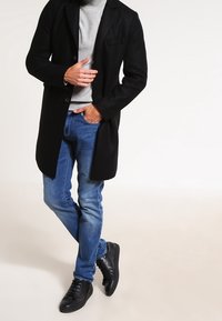 Black wool blend coat with a tailored fit, gray crew neck sweater, blue slim-fit jeans, and black lace-up sneakers.