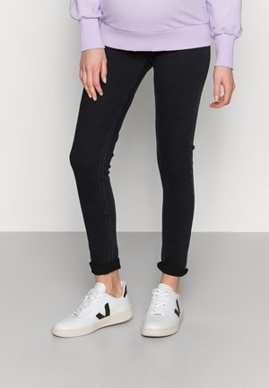 Persona que lleva vaqueros negros ajustados remangados en los tobillos, zapatillas blancas con logo negro y una camiseta de manga larga de color lila claro.