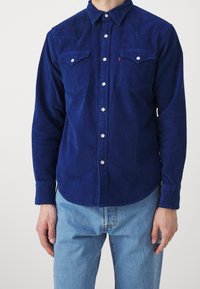 Kamelåtsknapp-up skjorta i mörkblått, har två framfickor, vita metallknappar och en rundad nederkant för en skräddarsydd passform.