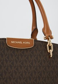 Sac à main marron foncé à motifs avec poignées en cuir marron clair et plaque en métal doré gravée Michael Kors.