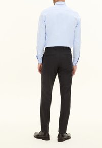 Helles Blaues Langarmhemd mit spitzen Kragen, kombiniert mit dunkelgrauen maßgeschneiderten Hosen. Schwarze Schuhe runden das Outfit ab.