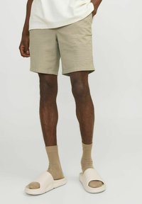 Haki šorti ar teksturētu audumu, virs ceļgaliem, kopā ar bēšām zeķēm un gaismas krāsas čībām. Vienkāršs dizains, bez rakstiem.