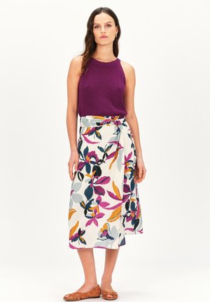 Haut sans manches violet ; jupe portefeuille longueur genou avec un motif floral multicolore sur un fond clair ; sandales plates marron.