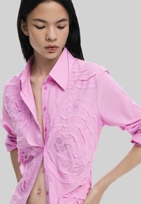 Roosa pikkade varrukatega särk nööpidega kraega, millel on tekstuuriga laine tikand ja avatud esiosa, esitleb mugavat istuvust ja kerget kangast.