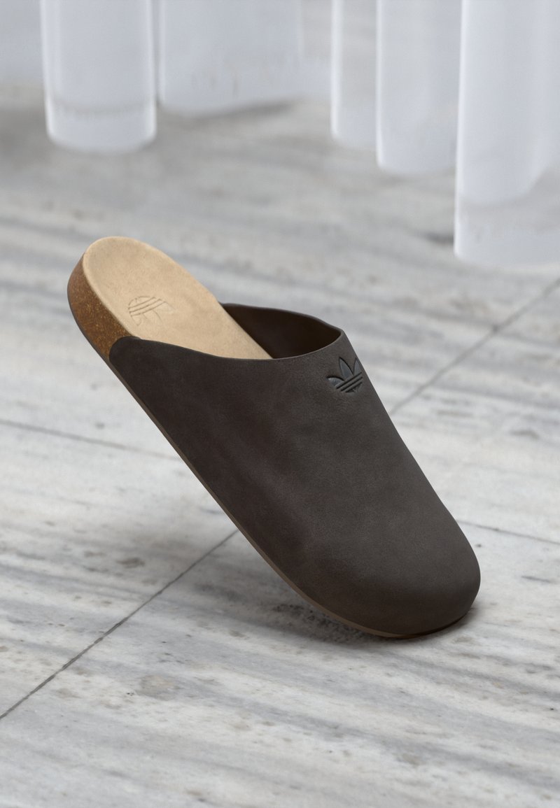 Temno sivi natikač z gladkim zgornjim delom, pluto podplatom in vtisnjenim logotipom. Ima zaobljen nos in minimalistični dizajn.