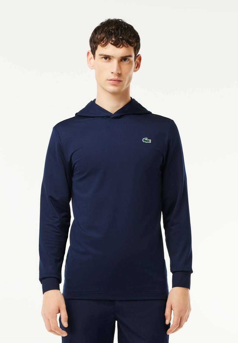 Marinblå långärmad hoodie i slät tyg, med en framficka i kängurustil och en grön broderad logotyp på bröstet.