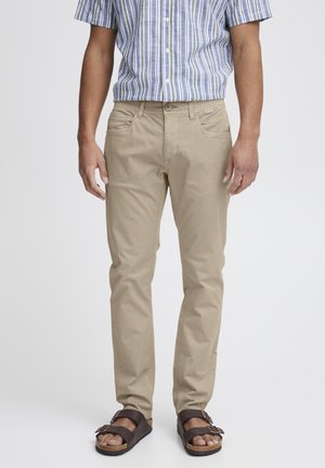 Beige cotton trousers with a straight fit and side pockets, paired with brown sandals. The shirt has blue and yellow vertical stripes.