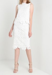 Vit spets tvådelad outfit med en ärmlös topp med scalloped kanter och en penningkjol med blommönster och fransat fåll.