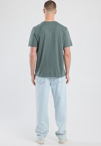 Green cotton t-shirt with a round neckline, short sleeves, and straight cut, paired with light blue loose-fit jeans and white sneakers.