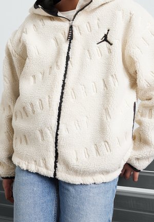 Weiße Fleecejacke mit erhabenem „JORDAN“-Muster, schwarzem Reißverschluss und Logo. Sie hat eine lockere Passform und eine Kapuze. Verfügt über Seitentaschen.