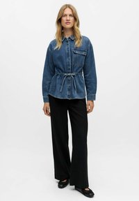 Denim krekls kleita ar savilktu jostasvietu, gariem piedurknēm un krūšu kabatu, apvienota ar melnām svītrainām biksēm un melnām plakanām kurpēm.