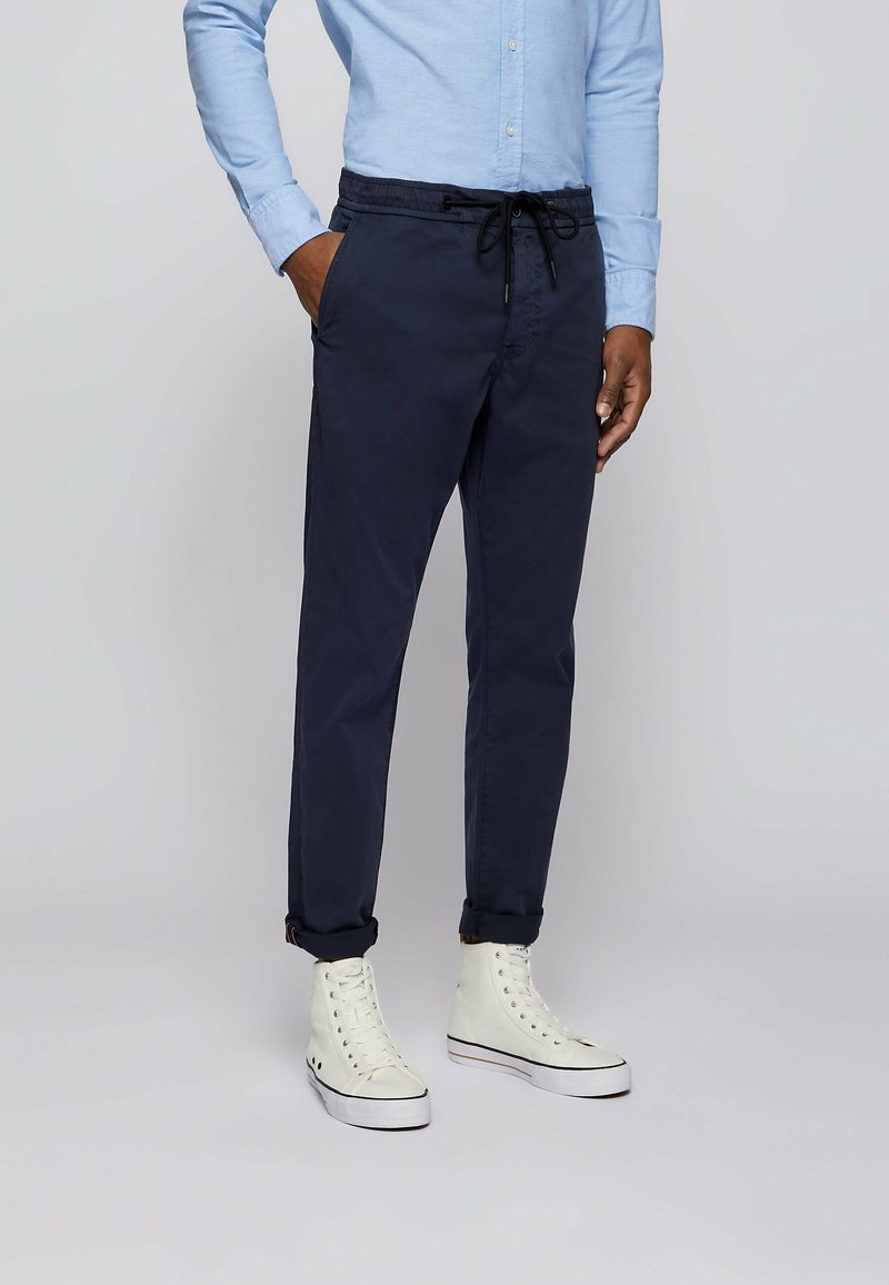 Marinblå taperade byxor med elastisk midja och dragsko; i kombination med vita högstövlar; slät tyg; uppvuxna fållar.