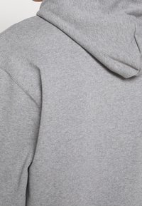 Sweat-shirt gris à capuche, présentant une texture douce et un design décontracté. Cordon de serrage ajustable et coutures visibles.