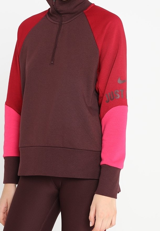 Le sweat-shirt Nike présente un col montant avec une fermeture éclair, un corps de couleur bordeaux foncé, des manches rouges et roses, et le texte « JUST DO IT » en gris sur le bras.