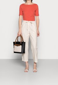 Top rosso a maniche corte, pantaloni alta vita beige e tacchi con cinturini trasparenti. Borsa tote nera con tasca frontale rosa e manici marroni.