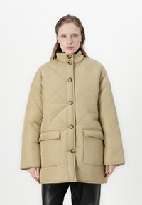 Beige prošívaná bunda s vysokým límcem, velkými předními kapsami a zapínáním na knoflíky. Má volný střih a hladkou texturu.