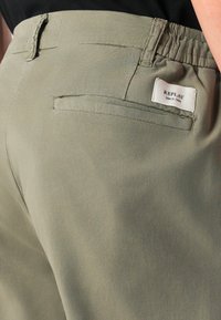 Pantaloni khaki con vita elastica, dotati di una tasca posteriore e di un piccolo etichetta del marchio. Texture morbida e liscia con un design semplice.