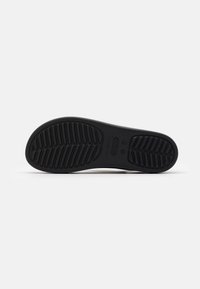 Semelle noire en caoutchouc d’une chaussure avec des motifs de bande de roulement texturés pour l’adhérence, affichant le nom de la marque "Crocs" au centre.