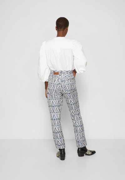 Blusa branca com mangas bufantes, combinada com calças azuis e brancas com padrão, de cintura alta, e sapatos pretos com riscas.