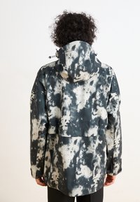 Wodoodporna kurtka z czarno-białym wzorem tie-dye, z kapturem, regulowanymi sznurkami i luźnym krojem.