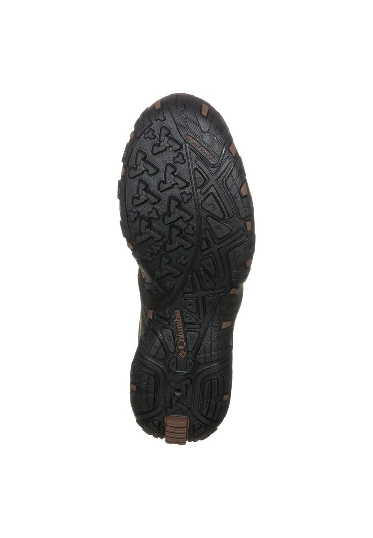 Suela de zapato de goma negra con un patrón de banda de rodadura robusto que presenta elementos triangulares y rectangulares, marcada con "Columbia" en marrón.