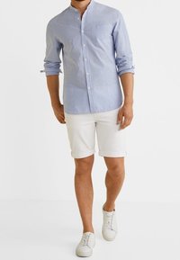 Camicia: a righe blu chiaro e bianche, maniche lunghe, colletto abbottonato. Pantaloni corti: bianchi, con risvolti. Calzature: sneakers bianche. Sfondo neutro.