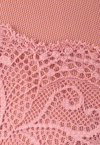 Tela de encaje rosa con patrones intrincados que presentan motivos florales y un fondo de malla delicada, mostrando textura y artesanía.