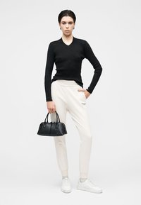 Top preto de manga comprida com textura canelada, calças jogger creme, ténis brancos e uma pequena mala preta com duas pegas. Design minimalista.