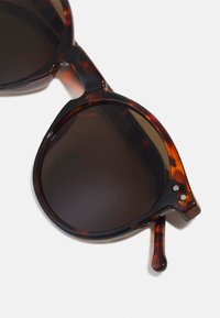 Ochelari de soare din tortoise cu lentile întunecate, formă rotundă și un ușor design cat-eye. Au accente din metal și un braț texturat.