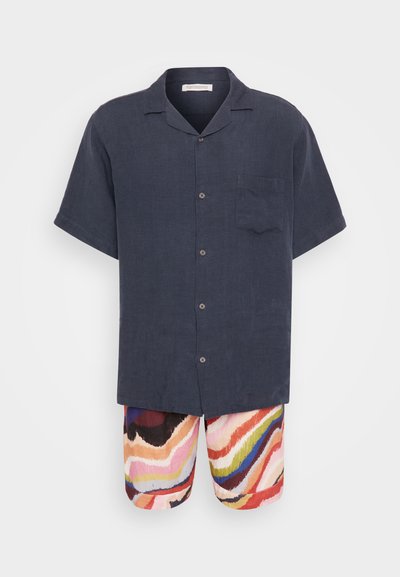 Camisa de lino azul marino de manga corta con un bolsillo en el pecho; pantalones cortos multicolores y estampados en olas de tonos rosa, amarillo, rojo y azul.