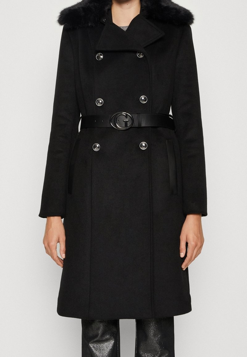 Zwart dubbelbreasted jasje met zilveren knopen, bontkraag en zwarte riem met ronde metalen gesp, gedragen over zwarte glanzende broeken.