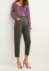 Top lungo a maniche con stampa floreale viola e scollatura arricciata, abbinato a pantaloni a vita alta verde oliva e scarpe con tacco rosa con cinturini.